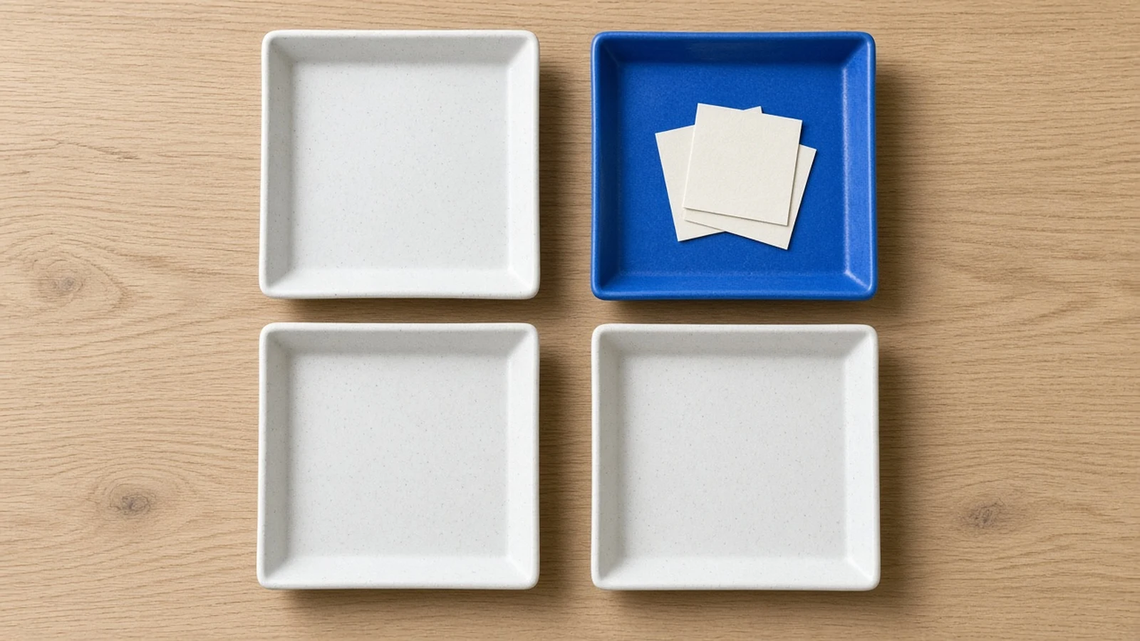 Four square trays in a two by two layout, the top right tray blue and holding paper cards