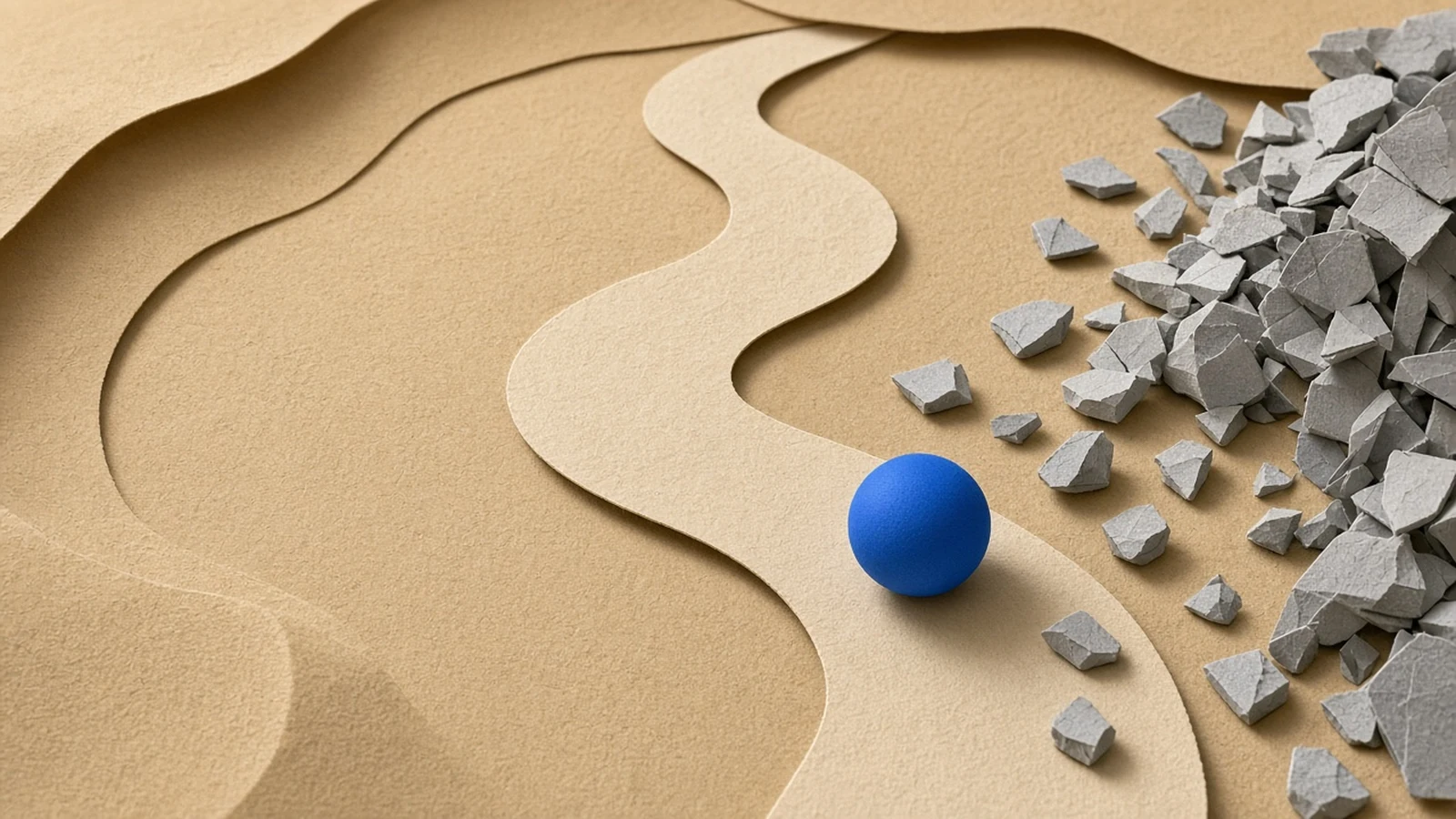 A winding paper path with a blue ball rolling along it and grey rock chips pushed to the side